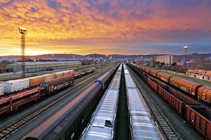 Blick auf Bahngleise mit unterschiedlichen Güterzügen bei Sonnenuntergang